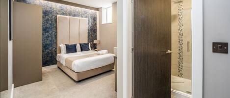 A modern bedroom with a large bed, a walk-in closet, and a shower area.