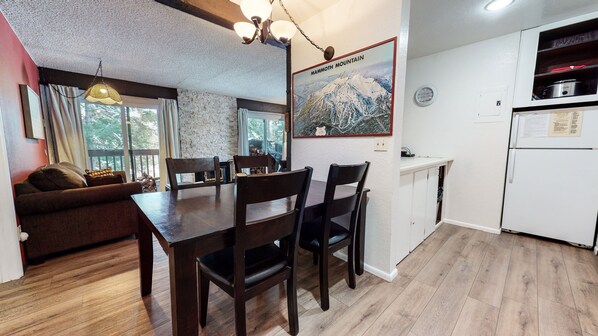 A cozy dining area with a wooden table and chairs, a sofa, and a large window with curtains. A map of Mammoth Mountain is displayed on the wall.