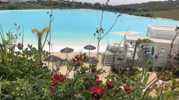 Ein Poolbereich mit Sonnenschirmen und Liegestühlen, mit Blick auf ein klares, blaues Schwimmbecken.