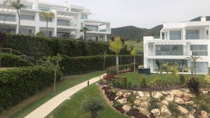 Ein moderner Wohnkomplex mit mehreren weißen Gebäuden, einem angelegten Garten mit Steinen und Sträuchern sowie einem gut ausgebauten Weg.