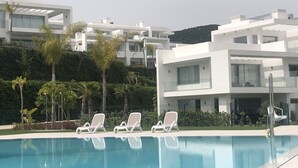 Ein moderner Poolbereich mit weißen Liegestühlen, einem klaren, blauen Pool und zeitgenössischer Architektur im Hintergrund.