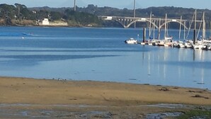Un puerto deportivo con barcos amarrados, un puente al fondo y una playa arenosa en primer plano.