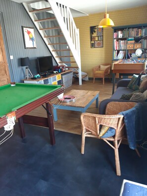 Una sala de estar con mesa de billar, un sofá, una estantería y una escalera.