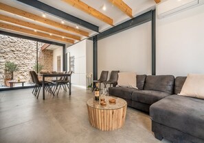 A modern living room with a stone wall, a dining area with a table and chairs, and a dark-colored sofa.