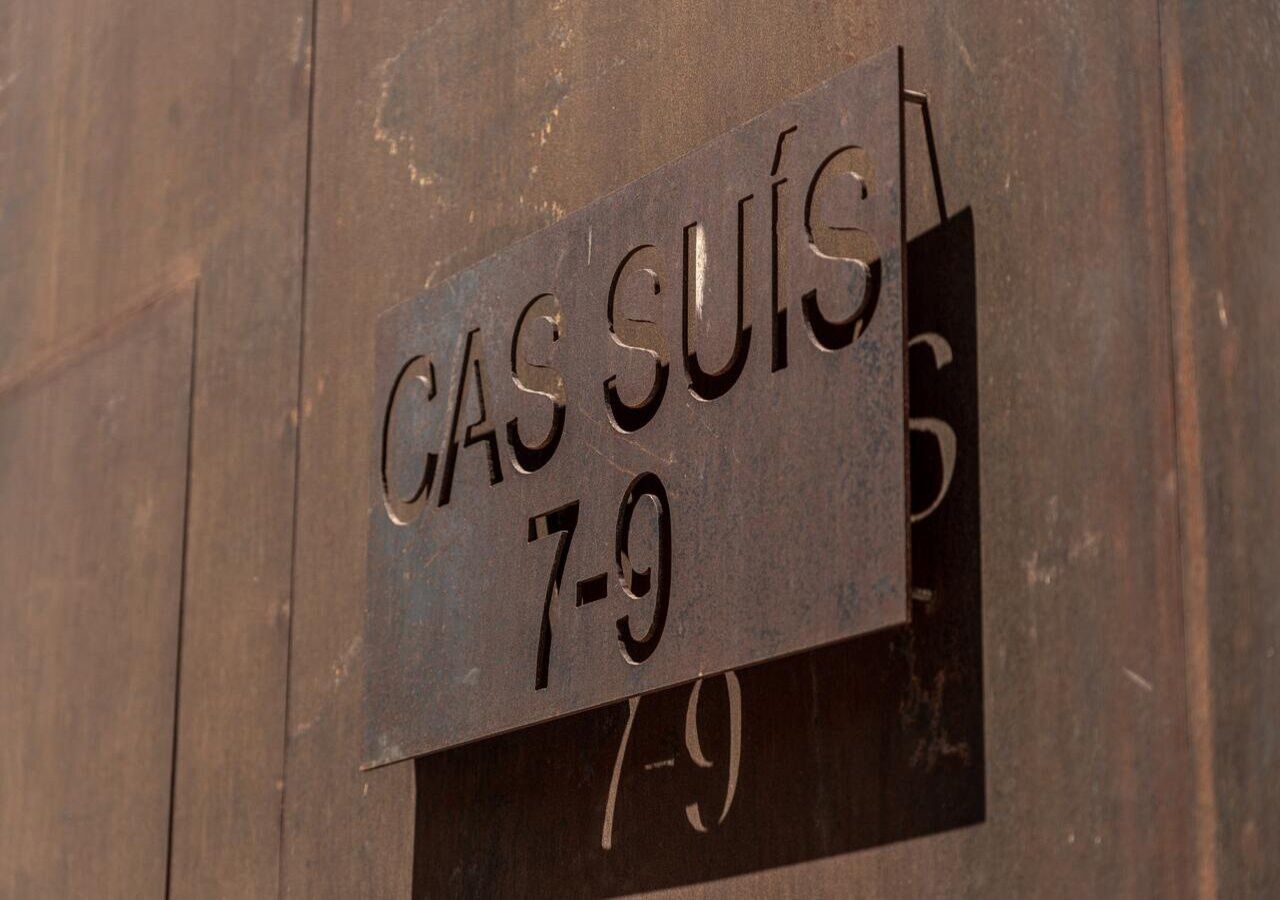 A metal sign with the text "CAS SUÍJA 7-9" mounted on a wooden wall.