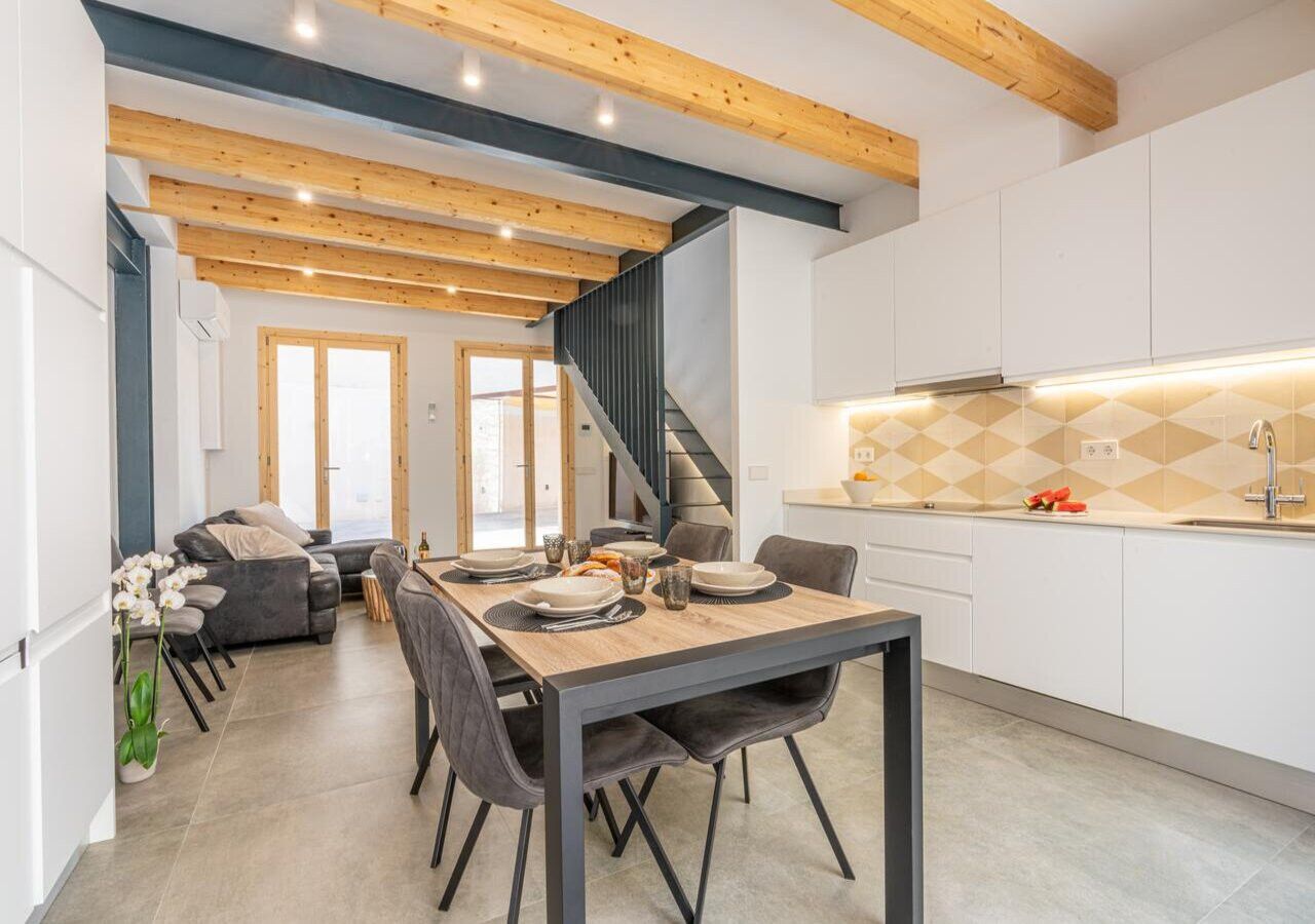 A modern kitchen with white cabinets, a wooden ceiling, and a dining area with a table set for four.