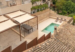A rooftop pool with a table and chairs, surrounded by stone walls and a view of neighboring buildings.
