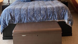 Una camera da letto con soffitto spiovente, un letto con copripiumino decorato, una ventola a soffitto, una finestra con persiane e un comodino con una lampada.