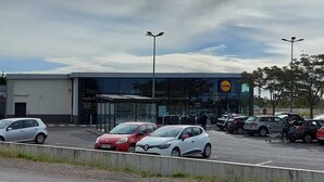 A parking lot with several cars, a building with a visible logo, and a clear sky. - Villa en Location Près des Plages (Saint-Brès)