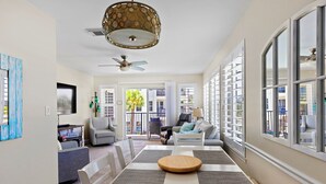 A spacious living room with a dining table, a ceiling fan, and large windows. - Poolside Villas DUNES AWAY, End Unit, VIEWS! Gulf and East Pass, 2 bdr/2ba, pool (Destin)