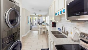 A modern kitchen with a built-in washer and dryer, a large window, and a dining area with a view. - Poolside Villas DUNES AWAY, End Unit, VIEWS! Gulf and East Pass, 2 bdr/2ba, pool (Destin)