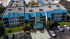 A multi-story hotel with a parking lot, located near a beach with clear blue waters and sandy shores. - Poolside Villas DUNES AWAY, End Unit, VIEWS! Gulf and East Pass, 2 bdr/2ba, pool (Destin)
