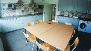 Een compacte keuken met een betegelde spatwand, een magnetron en een wasmachine. Er staat een eettafel met stoelen en een kleine televisie op het aanrecht.