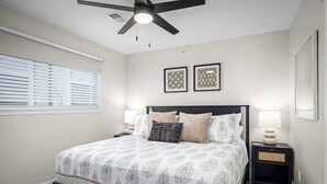 A bedroom with a bed, two bedside tables, a ceiling fan, and wall-mounted artwork. - River Access | Shared Pool & Spa | Close to Town! (New Braunfels)