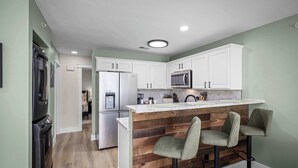A kitchen with white cabinets, a wooden island with bar stools, stainless steel appliances, and a tiled backsplash. - River Access | Shared Pool & Spa | Close to Town! (New Braunfels)
