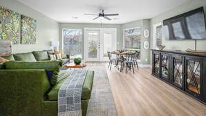 A living room with a green sofa, a coffee table, and a TV on a cabinet. - River Access | Shared Pool & Spa | Close to Town! (New Braunfels)