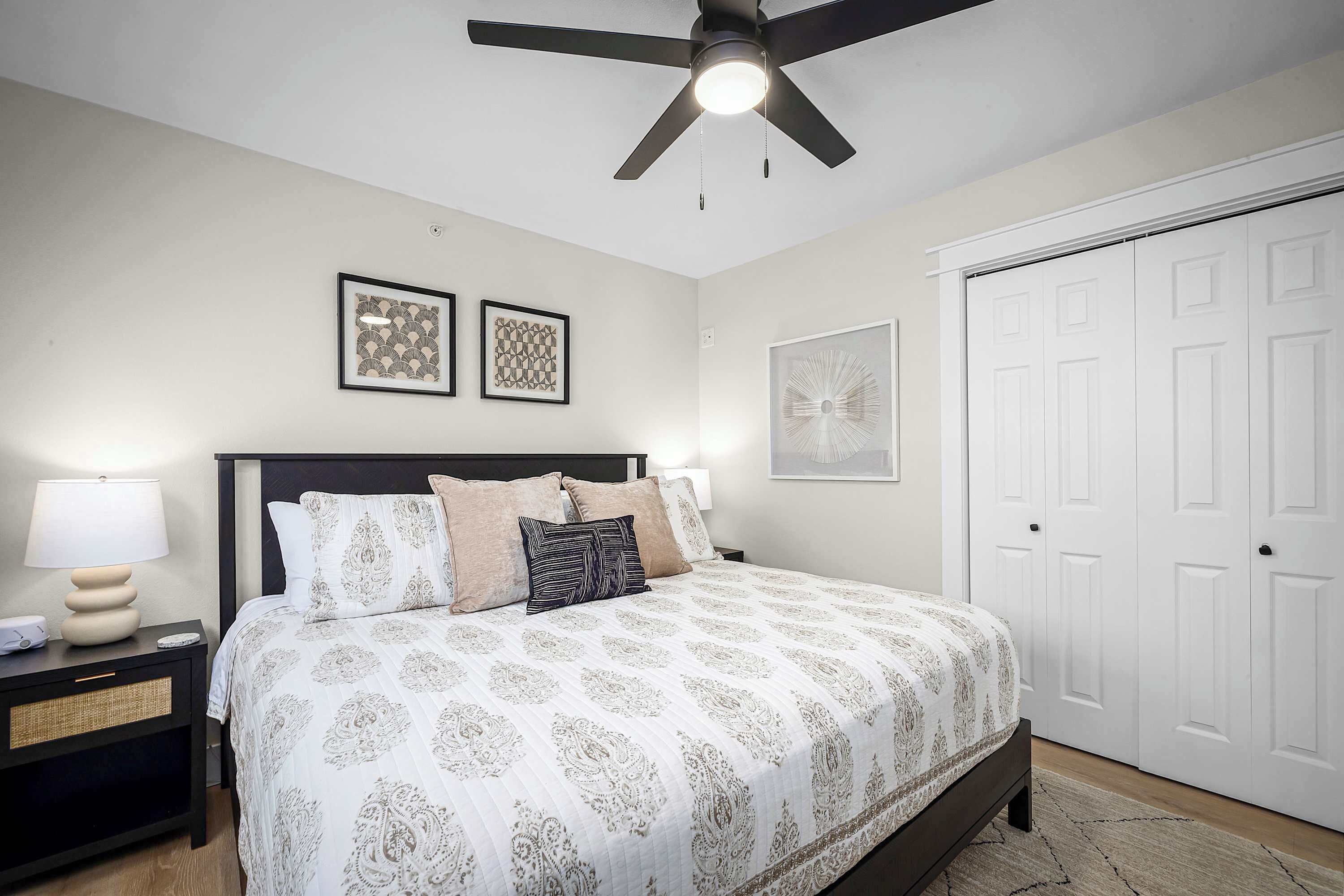 Une chambre à coucher avec un lit, une table de chevet, un ventilateur de plafond et une porte blanche.