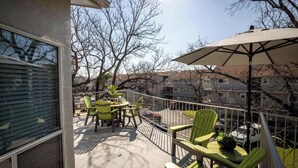 A balcony with green chairs, a table, and a large umbrella. - River Access | Shared Pool & Spa | Close to Town! (New Braunfels)
