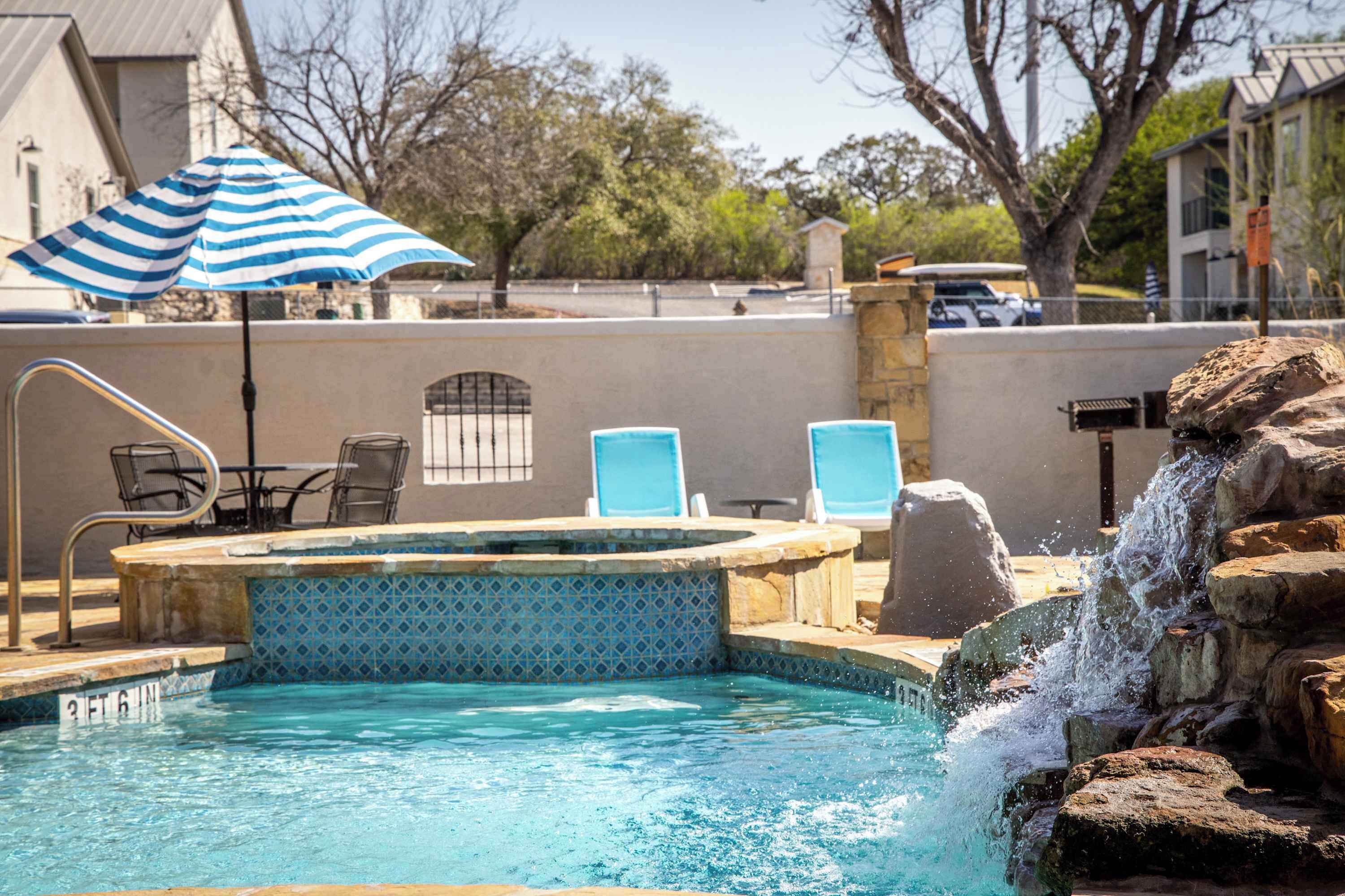 Une piscine avec un jacuzzi, des chaises bleues et une cascade décorative.