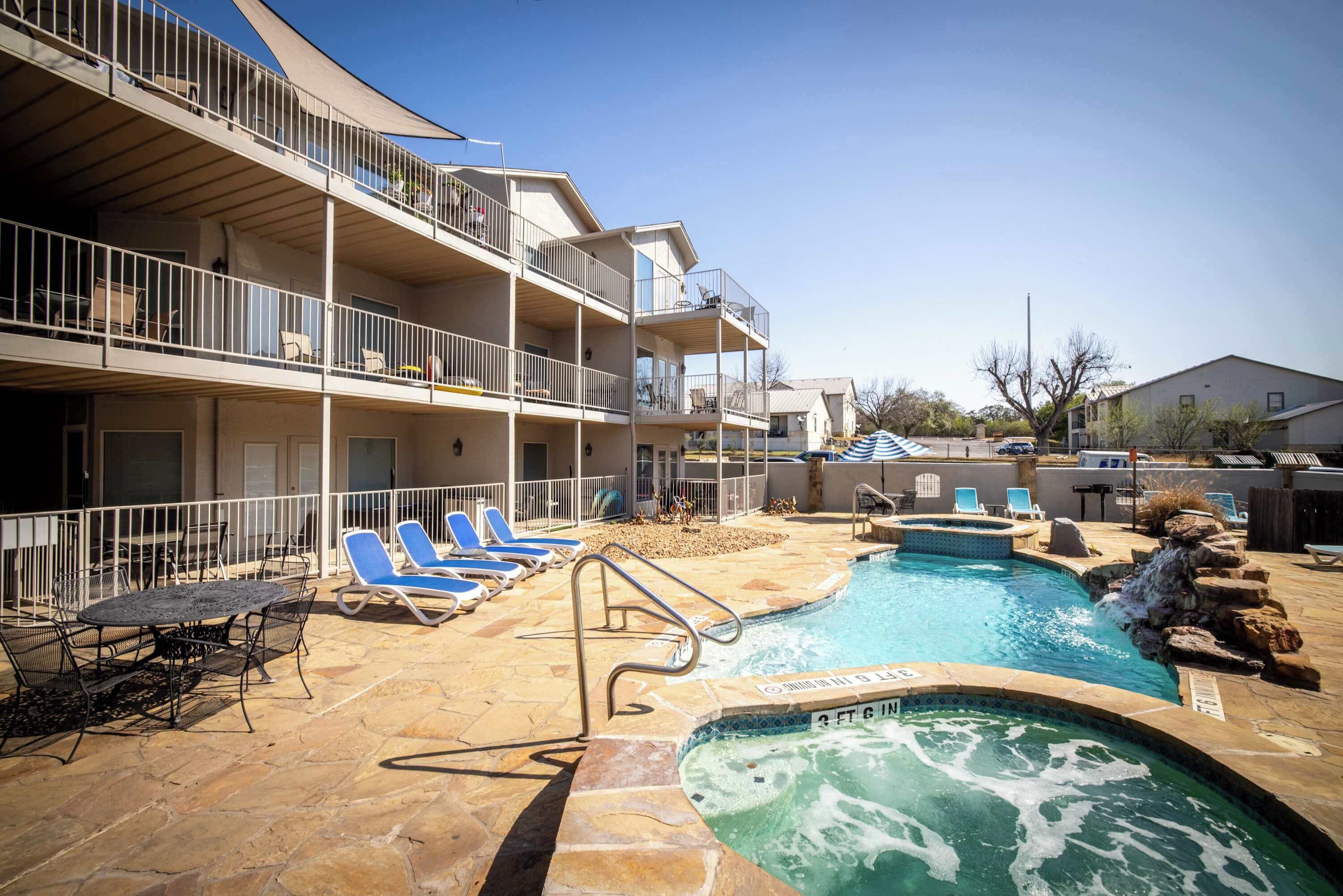 A multi-story building with balconies, a swimming pool with lounge chairs, and a hot tub.