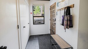 A narrow hallway with a door, a window, a coat rack, and a small table.