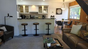 Een moderne keuken met een bar, een eettafel met stoelen, een leren bank en een bijzettafeltje met een plant.