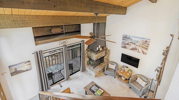 A cozy living room with a stone fireplace, a ceiling fan, and a TV mounted on the wall.