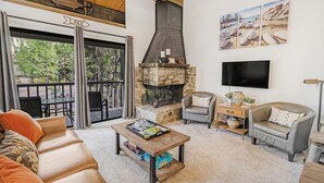 A cozy living room with a stone fireplace, comfortable seating, a television, and a view of the outdoors.