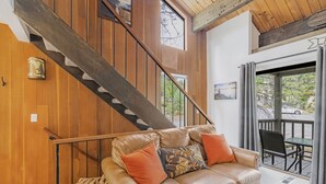 A modern interior with a leather sofa, wooden walls, a staircase, and a balcony with outdoor seating.