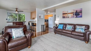 A spacious living area with a brown leather couch, a dining table, and a kitchen in the background.