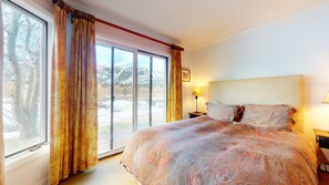 A bedroom with a large bed, a sliding glass door leading to a snowy outdoor area, and a nightstand with a lamp.