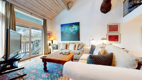A cozy living room with a large window, a flat-screen TV, a sofa, a coffee table, and a mounted animal head.