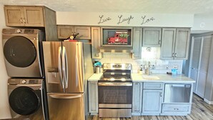A kitchen with a stainless steel refrigerator, double oven, and a washing machine. There is a decorative sign above the sink that reads "Live Laugh Love".