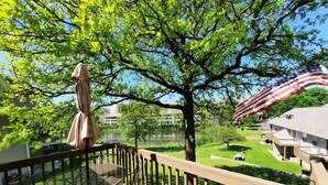 A balcony with a table and chairs, an American flag, and a view of a lake and buildings.