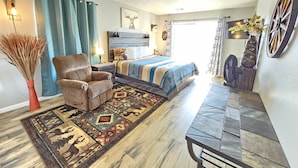 A cozy bedroom with a bed, a chair, a rug, and a fan.