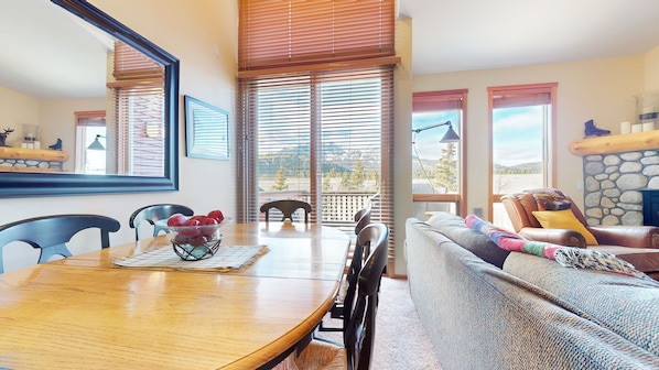 Un salon chaleureux avec une table à manger en bois, un canapé recouvert de plaids colorés et une cheminée.