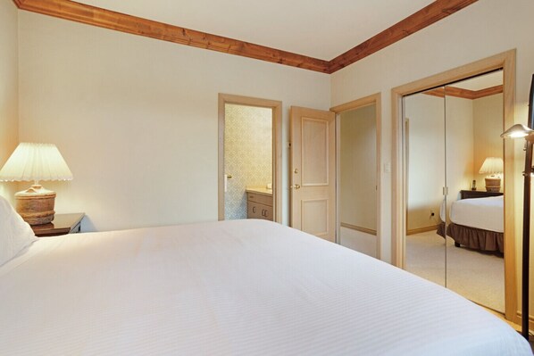 A hotel room with a large bed, a nightstand with a lamp, a wardrobe, and a mirror.