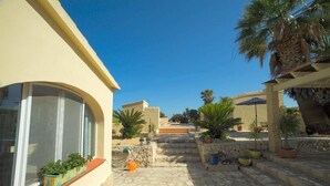 Un patio con suelo de piedra, plantas en macetas y un cielo azul despejado.