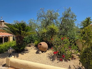 A garden with a variety of plants, a large decorative pot, and a building with a tiled roof.
