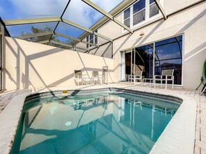 Una piscina con un recinto in vetro, circondata da un patio con sedie e tavolo.
