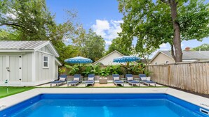 Un jardin avec une piscine, des chaises longues et des parasols.