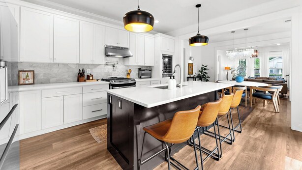 Une cuisine moderne avec des meubles blancs, un grand îlot central doté de tabourets et des luminaires suspendus.