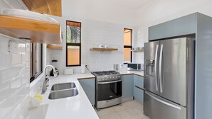 Une cuisine moderne avec des carreaux blancs, des appareils électroménagers en acier inoxydable, une cuisinière à gaz et un réfrigérateur.