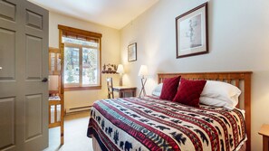 Un dormitorio con cama, ventana, puerta y mesita de noche.