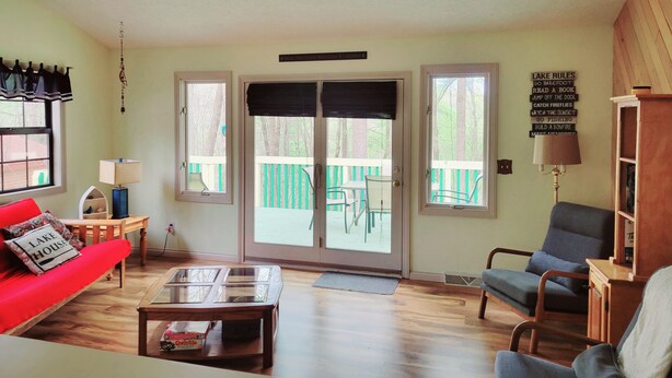 A living room with a red couch, a glass-top coffee table, and a blue armchair. There are two windows with blinds, a ceiling fan, and a sign on the wall. - Cabin Near Dale Hollow Lake (Byrdstown)