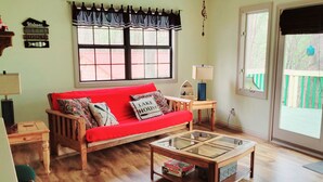 A cozy living room with a red sofa, wooden coffee table, and a window with a view of a green fence. - Cabin Near Dale Hollow Lake (Byrdstown)