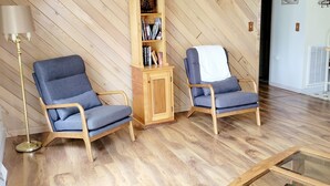 A living room with two blue armchairs, a wooden bookshelf, a floor lamp, and a glass coffee table. - Cabin Near Dale Hollow Lake (Byrdstown)