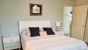 A neatly made bed with striped bedding, a bedside table with a lamp, and a framed picture on the wall. - Cabin Near Dale Hollow Lake (Byrdstown)