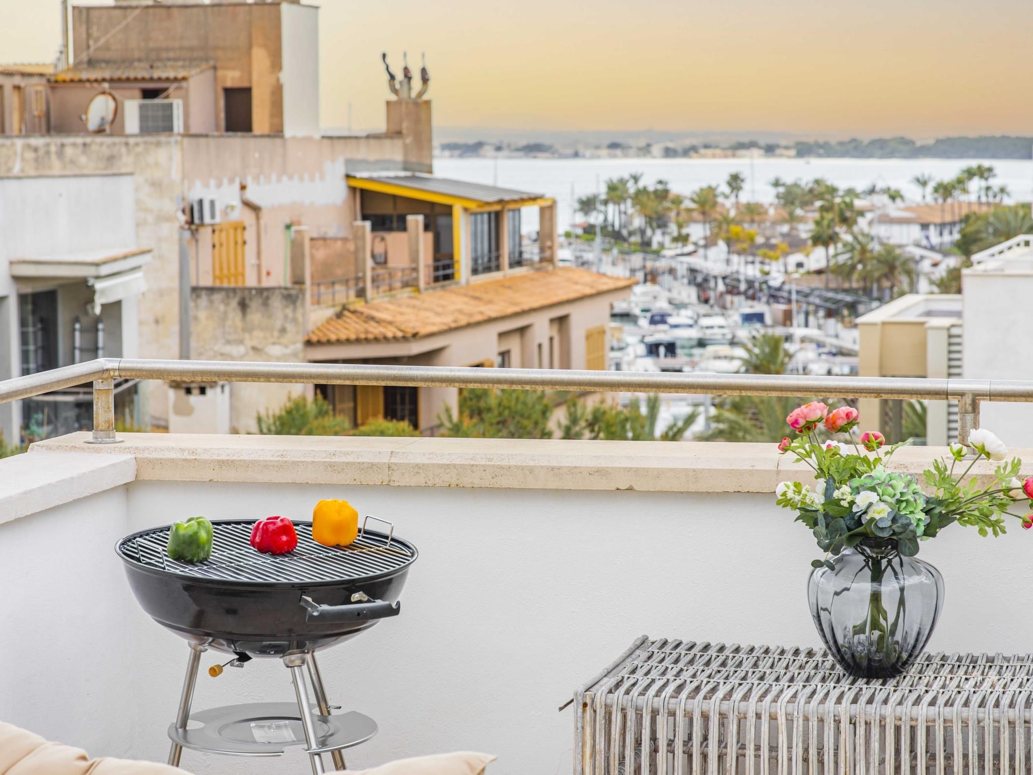 A balcony with a grill, a vase with flowers, and a view of a marina and buildings.