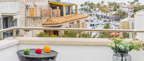A balcony with a grill, a vase with flowers, and a view of a marina and buildings.